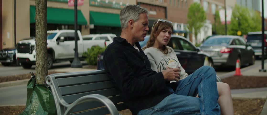 A father and daughter eat on the bench