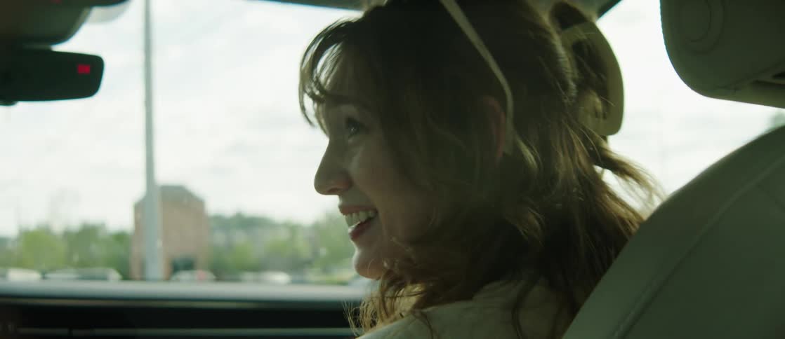 Portrait of a young woman in the front seat of a moving car smiling and opening her mouth with surprised facial expression