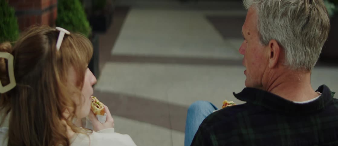 Man and woman seen from the back sitting eating a sandwich