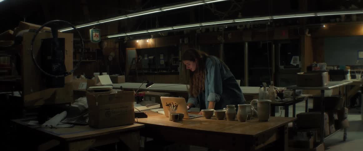 A woman is working on a laptop in a studio or workshop at night