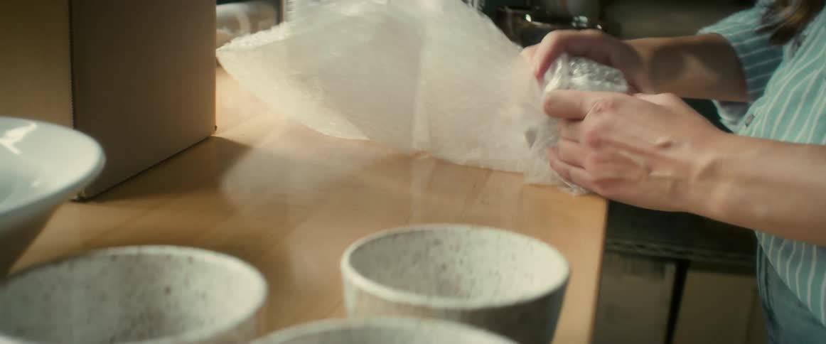 A woman wrapping a ceramic cup in bubble wrap