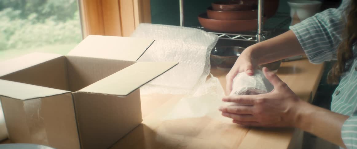 A woman wrapping an object with bubble wrap then placing it in a cardboard box