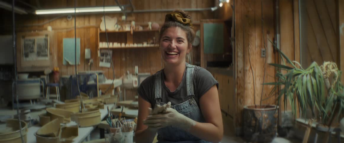 Woman indoors smiling while her hands are covered in clay