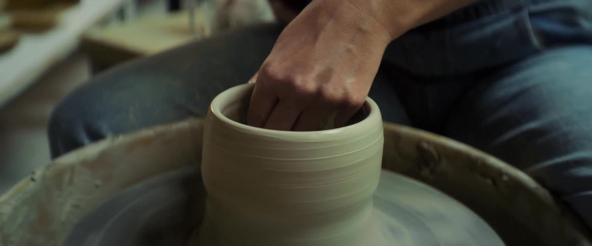 A woman shapes clay on a spinning wheel