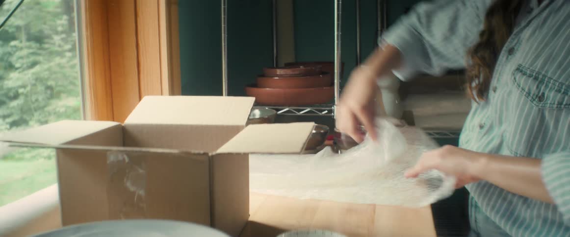 A woman is packing ceramic bowls on a cardboard box