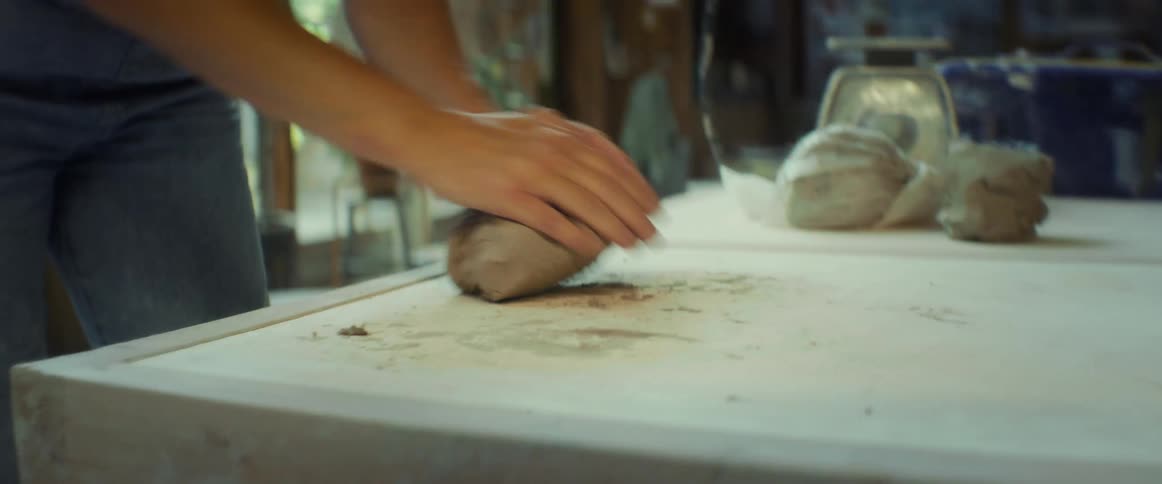 A woman kneading a ball of clay with her hands on a table