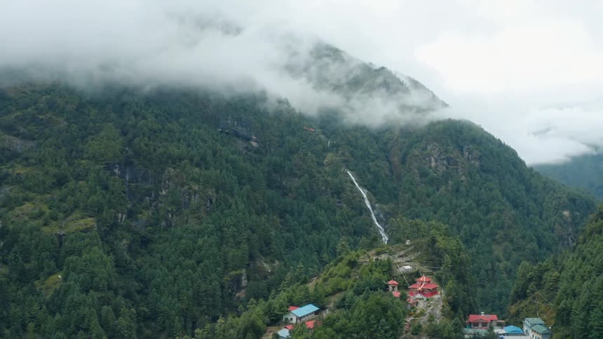 Aerial panorama of a helicopter flying amid mountains and above a village on a cloudy day