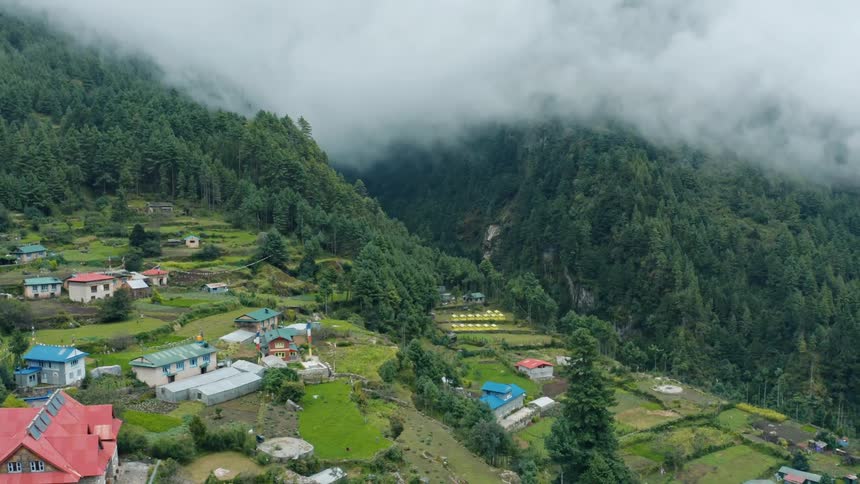 A rural village on the side of a mountain near a forest covered by fog