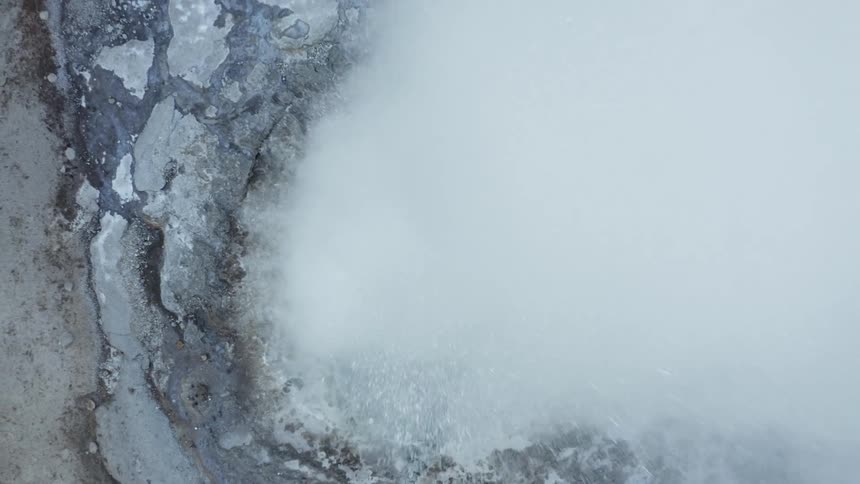 Geyser erupts in rough terrain filling the air with water and vapor