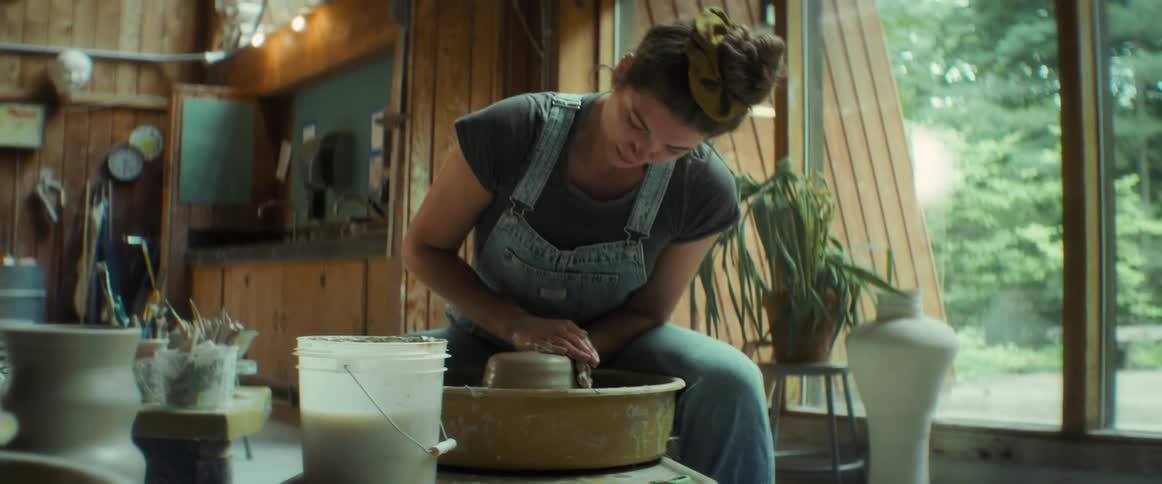 A young woman works a lump of clay on a spinning wheel