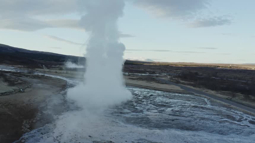 An aerial view of a geyser eruption with steam and water shooting upwards