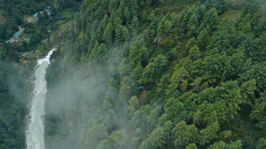 A river runs between a forested mountain and a small rural community