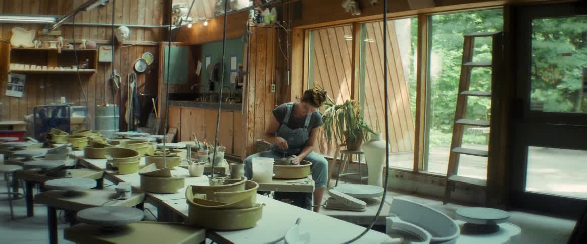 A woman in a workshop sculpting clay in a pottery wheel