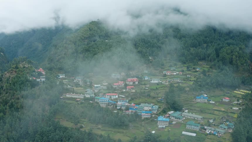 An aerial view of a small town in a lush green valley with a river under the clouds