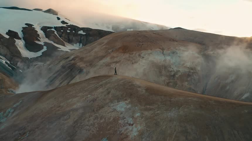 Person walking on a cliff with mountains around on a foggy day