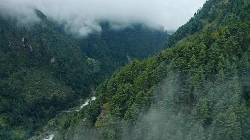 Bright roofed houses line riverbank in narrow valley between forested mountains