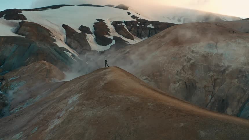 Aerial panorama of a man on the peak of a mountain cliff in winter on a morning