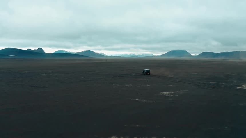 Jeep driving on a desert land with mountains around on a cloudy sky day