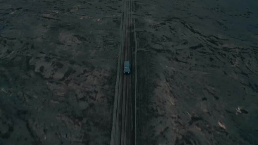 Black car driving on a volcanic dirt road with mountains around on a cloudy day