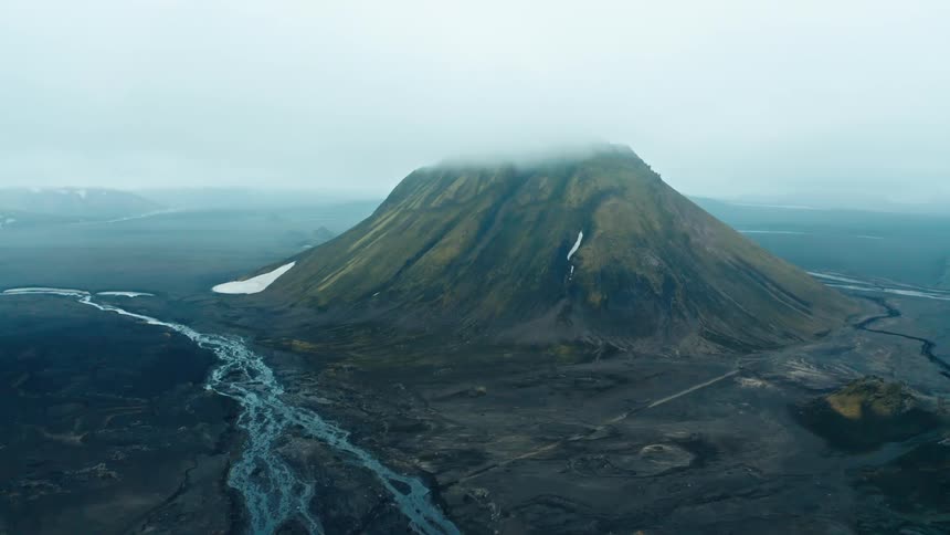 Fog hangs over a mountain sitting next to a plain and river