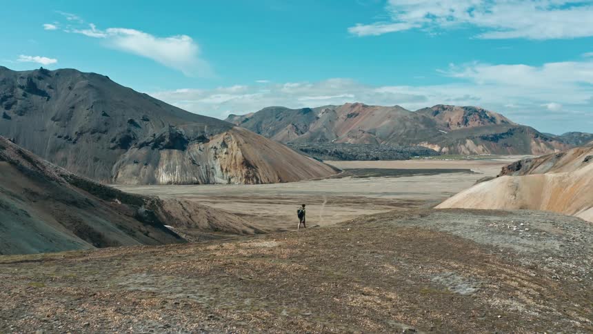 Male backpacker hikes along mountain top path overlooking valley