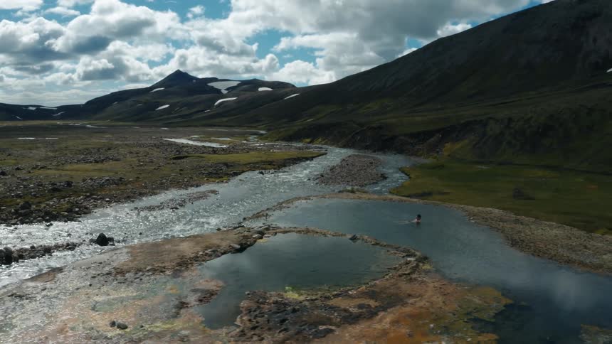 Man lying in a lake with a river in front of him and surrounded by mountains