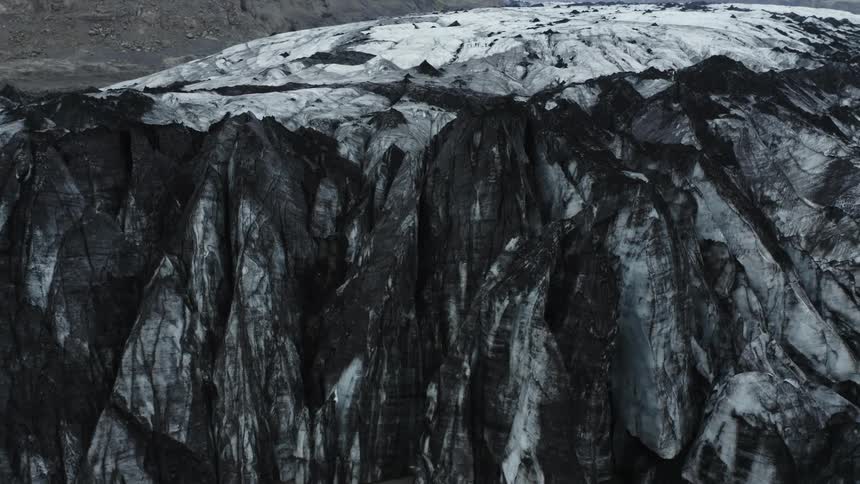 Aerial panorama of mountain with black rocks on the edge of a gray lake