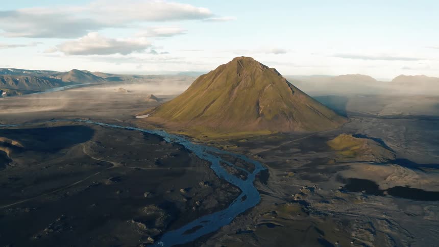An aerial view of a solitary mountain by a flat volcanic landscape and a winding river