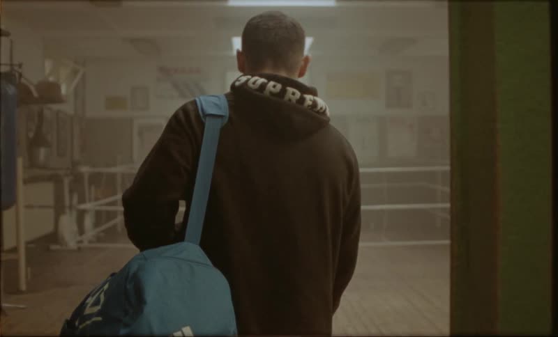 Follwing a boxer with a blue duffel bag entering a boxing gym
