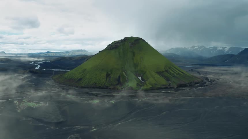 A green mosscovered mountain against a dark volcanic landscape