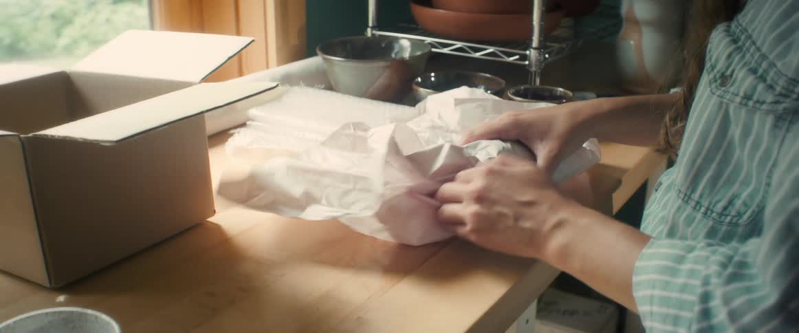 A woman wraps a clay vase in paper