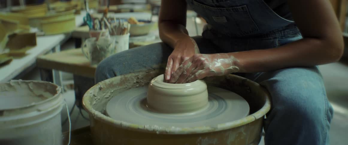 A black woman sculpts clay on a spinning wheel