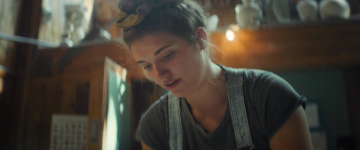A woman is kneading clay on a wooden table in a rustic workshop