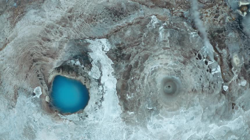 View from above of a steamemitting crater and a blue thermal lake