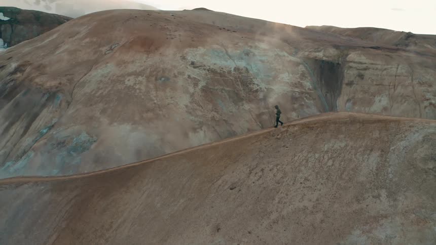 A man walking along the crest of a mountain as steam rises from below