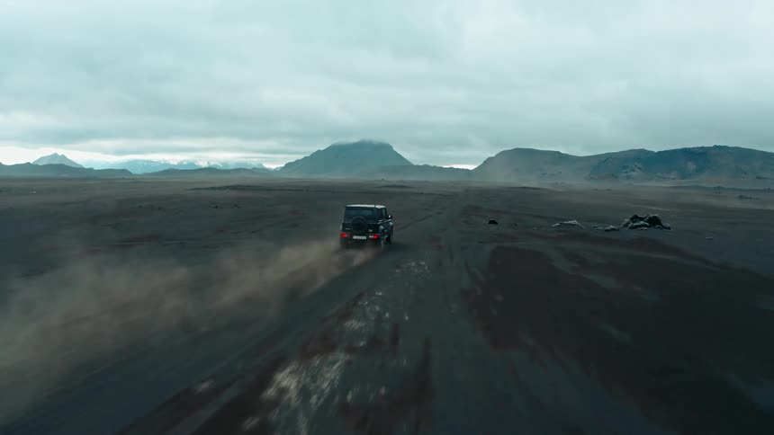 A vehicle drives across a blasted mountain valley