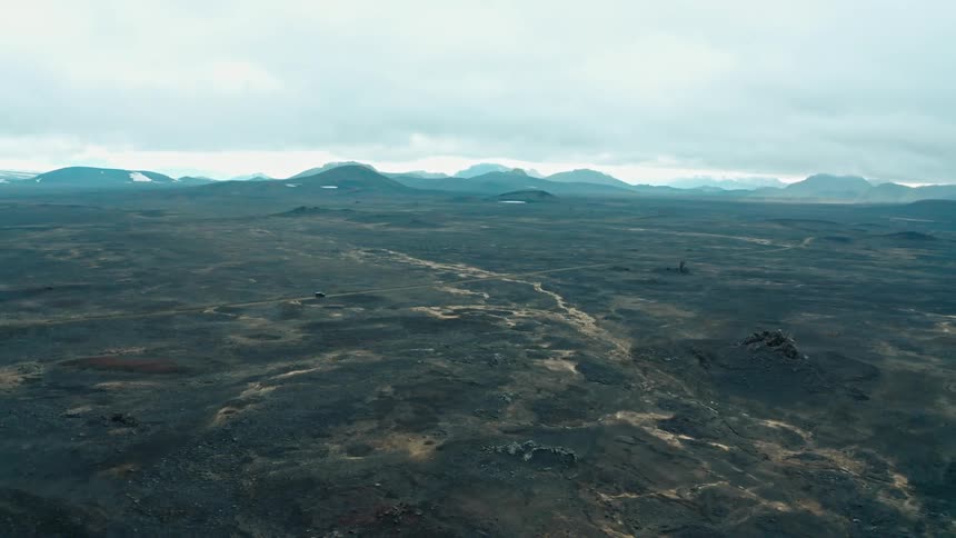 A vehicle drives on a road across a massive plain in a mountain valley