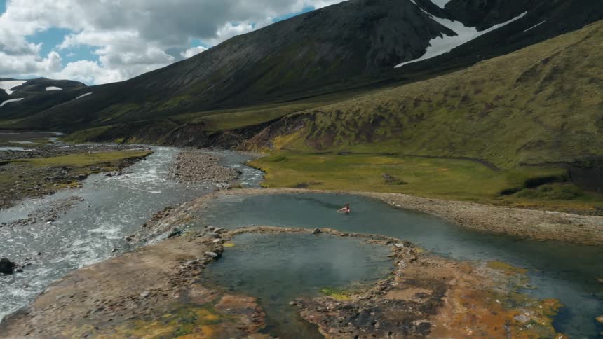 A white man bathes in a water next to a river and mountains