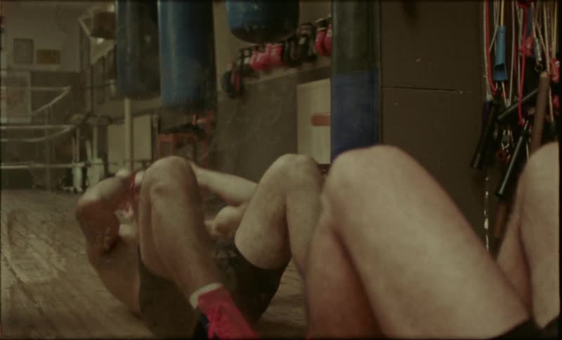 A shirtless boer does situps in front of a mirror at the gym