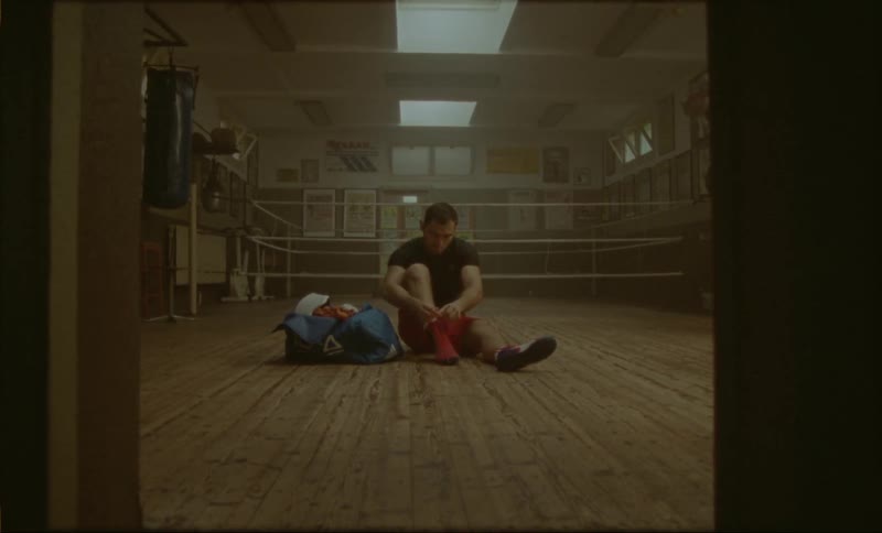 A boxer ties his boxing shoes near a boxing ring