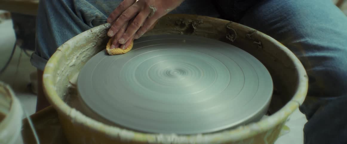Fingers of a woman with a loofah cleaning a clay pot production tool