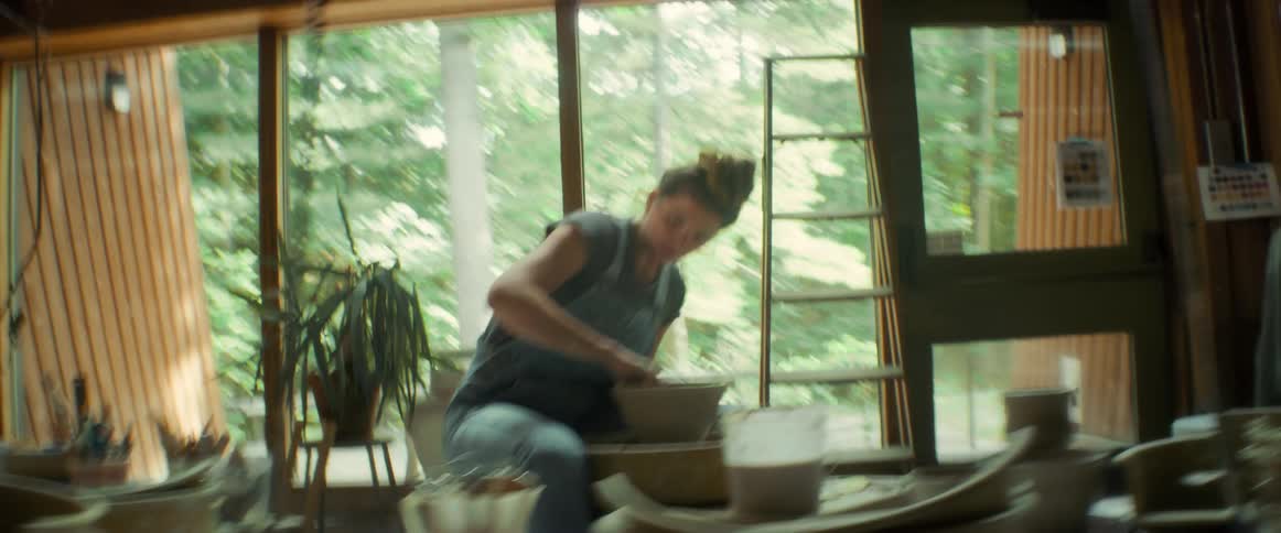 A woman in a workshop sculpting clay in a pottery wheel