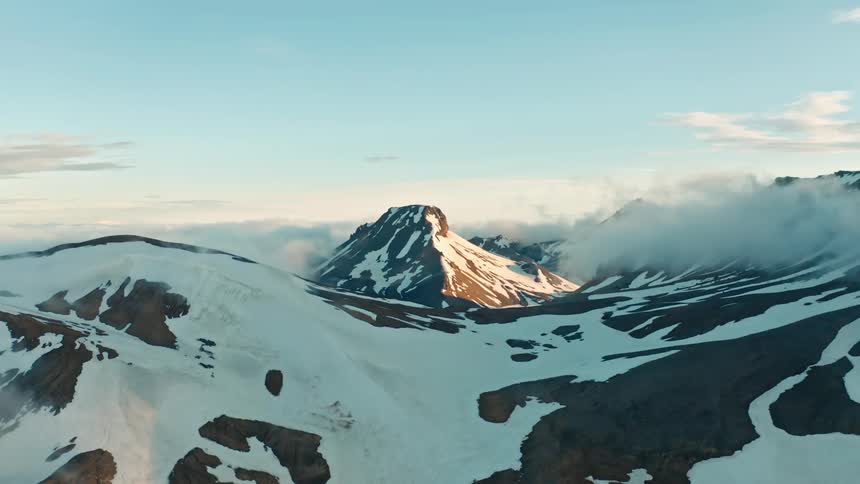 Aerial view of a snowcapped mountain peak with jagged ridges casting long shadows across the valley below