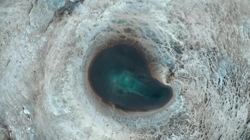 A geyser with clear blue water bubbling up from the earth