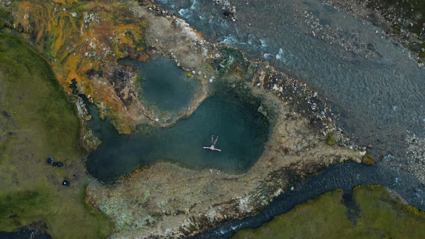Aerial scene of a man floating in a small lake with a river around it