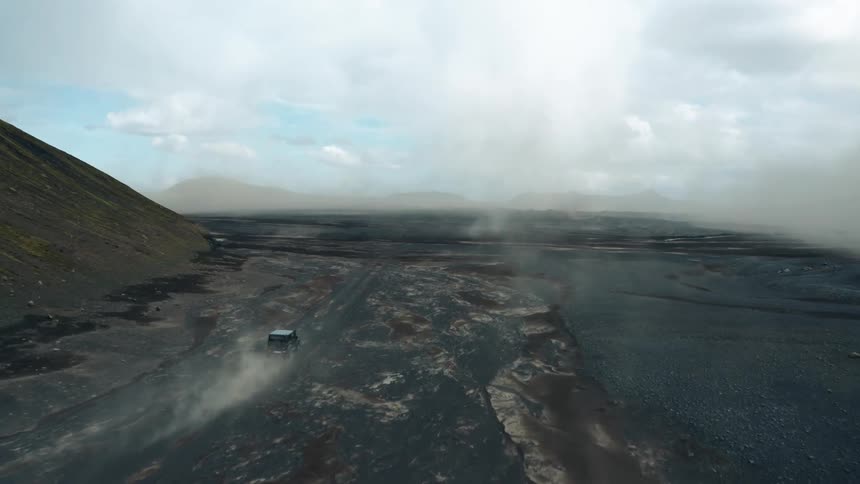 Aerial panorama of a black jeep traveling on rocky ground with mountains around it on a cloudy day