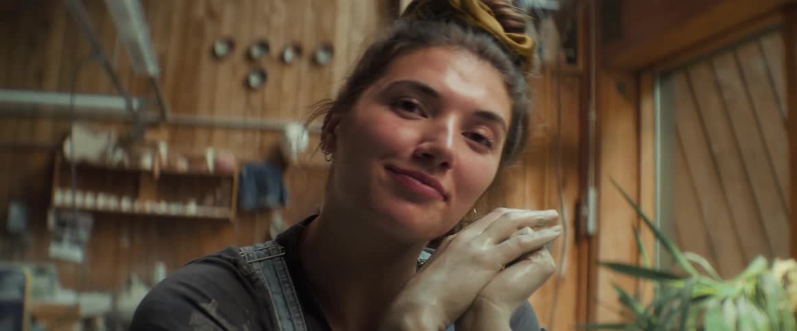 A young woman with dirty hands smiles while sitting in a room