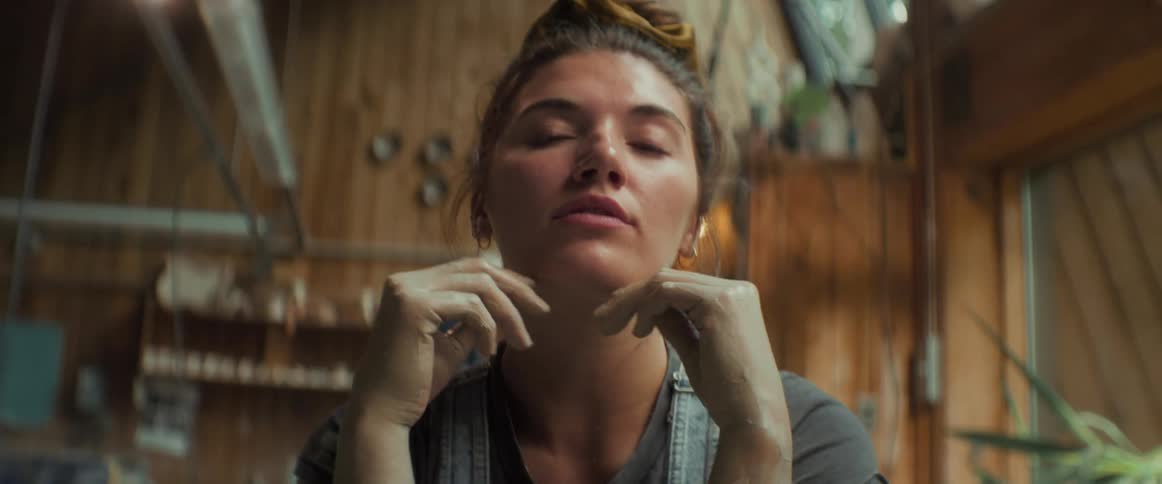 Portrait of a young woman sitting with claystained hands placing her face on her hands