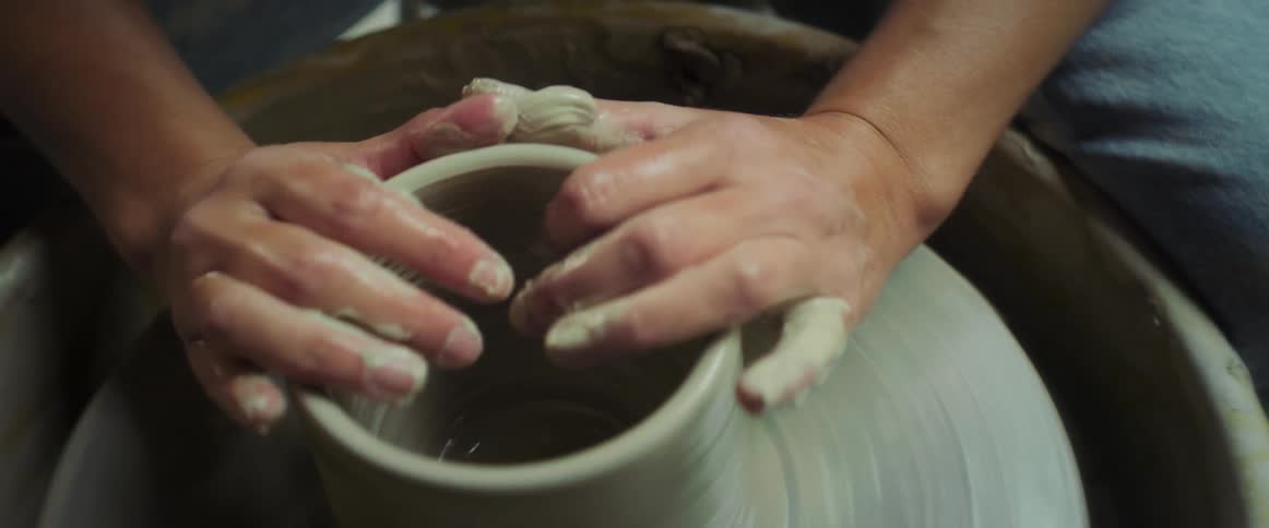 A woman carefully forms pottery on a spinning wheel