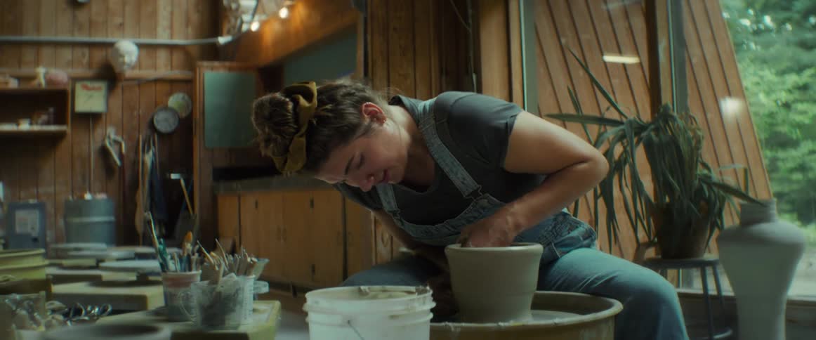 A woman in a denim apron is shaping clay on a pottery wheel